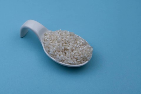 White ceramic spoon with white uncooked rice and blue background
