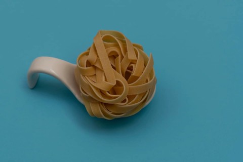 White ceramic spoon with spaghetti and blue background