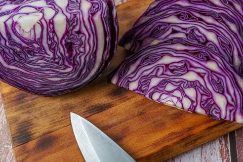 Close-up of a red cabbage or purple cabbage cut with a knife on a wooden board