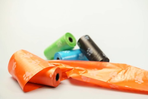 Rolls of biodegradable dog poop bags with paw print pattern unrolling on a white background