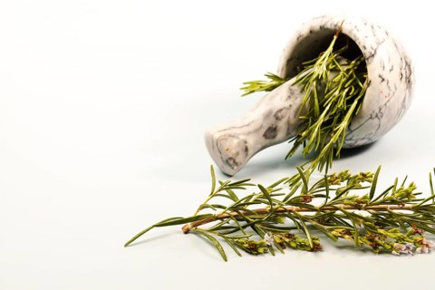 Fresh rosemary herb sprigs with flowers spilling from a marble mortar and pestle, ready for