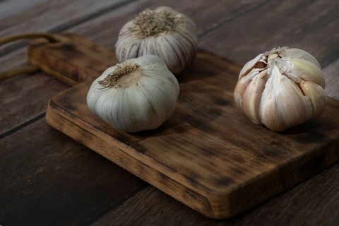 Whole and peeled garlic on wooden board and white background