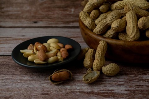 Peanuts in a wooden bowl and peeled peanuts on a plate with a spoonful of peanut butter