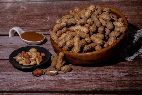 Peanuts in a wooden bowl and peeled peanuts on a plate with a spoonful of peanut butter