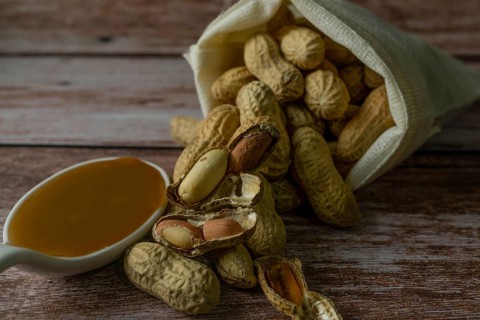 Peanuts in a raffia sack with a spoonful of peanut butter on a wooden bottom