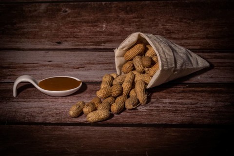 Peanuts in a raffia sack with a spoonful of peanut butter on a wooden bottom