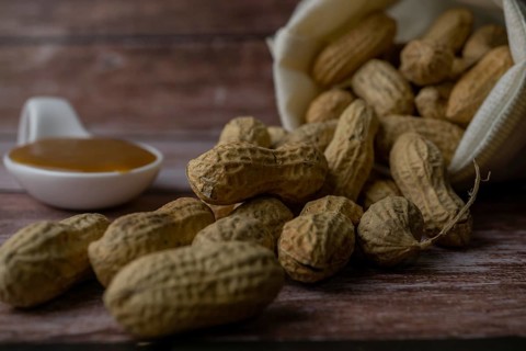 Peanuts in a raffia sack with a spoonful of peanut butter on a wooden bottom