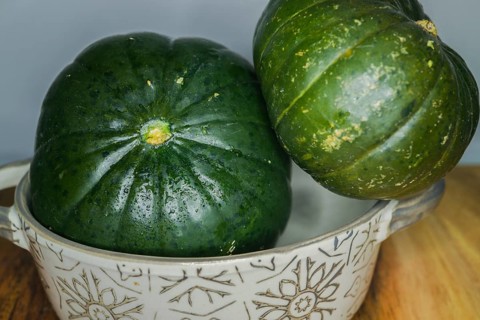 Green pumpkins in a ceramic bowl on wood and a white background
