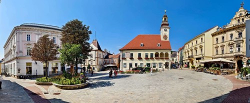 Panoramic view of a town square with historic clock tower and surrounding buildings under a clear