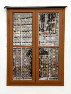 Window with decorative coin collection behind glass, framed by a simple wooden structure Mödling