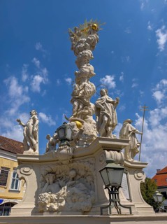 Baroque fountain with artistic sculptures under a slightly cloudy, blue sky Mödling Lower Austria