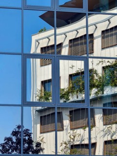 Reflection of a modern building with glass façade and greenery under a blue sky Mödling Lower