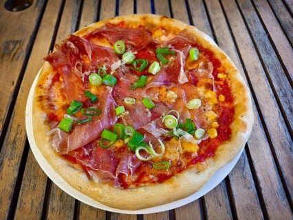 Pizza with ham and spring onions served on a table. Hearty and fresh with an Italian flavour