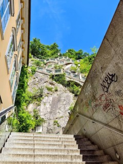 Modern stone staircase leads to a green rock under a clear sky, with graffiti stairs to the Graz