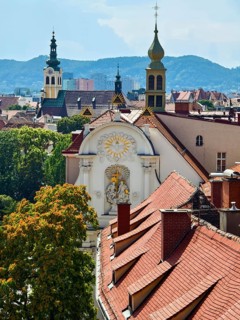 Panoramic view over the roofs of a historic city with church towers and mountains in the background
