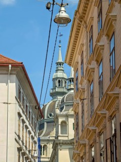 Historic buildings and a church tower under a blue sky, bustling urban atmosphere Landhaus Graz