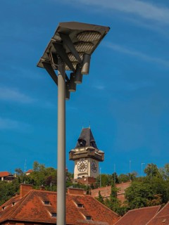 Clock tower behind a street lamp, surrounded by historic roofs and trees Graz Clock Tower Graz
