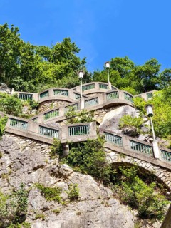 Stone wall with green railings and lamps on a steep, wooded slope under a blue sky Graz Styria