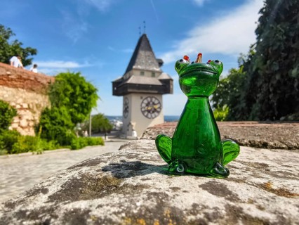 Green glass figure of a frog in front of historic clock tower