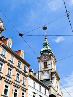 Detailed church tower rises above bourgeois buildings with a clear sky Herz Jesu Kirche Graz Styria