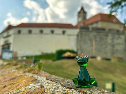 Glass figure of a frog king in front of a castle wall under a cloudy sky Riegersburg Styria Austria