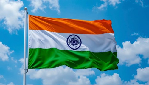 The Indian flag flutters against a bright blue sky dotted with puffy white clouds. A symbol of