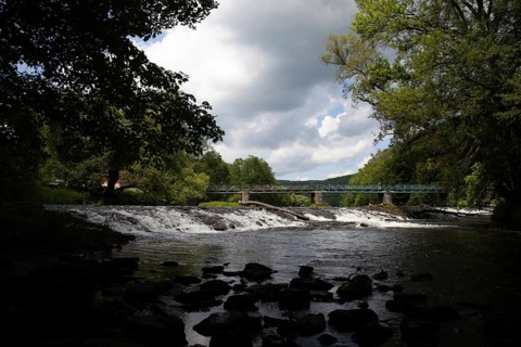A forested stretch of river with a bridge and waterfall under a cloudy sky Hardegg Weinviertel
