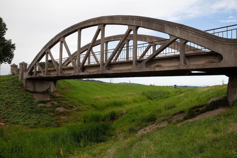 A concrete arch of the bridge stretches across a green meadow under a clear sky Perschling Flood