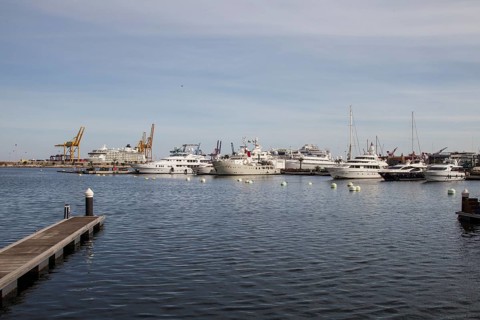 View of a busy harbour with yachts and industrial cranes in the background