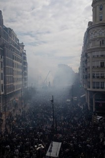 A large crowd gathers in a smoky city street MascletÃ¡ de Fallas