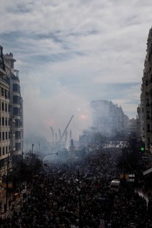 Dense crowds in the city with rising smoke and buildings MascletÃ¡ de Fallas