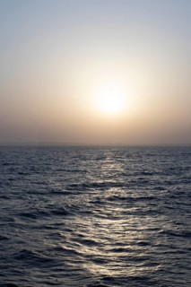 Background image, setting sun with silhouette of land, water surface in evening light, waves in the