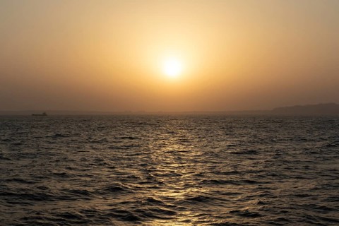 Background image, setting sun with silhouette of land, water surface in evening light, waves in the