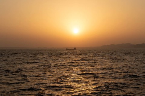 Background image, setting sun with silhouette of ship and land, water surface in evening light,