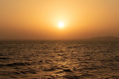 Background image, setting sun with silhouette of land, water surface in evening light, waves in the