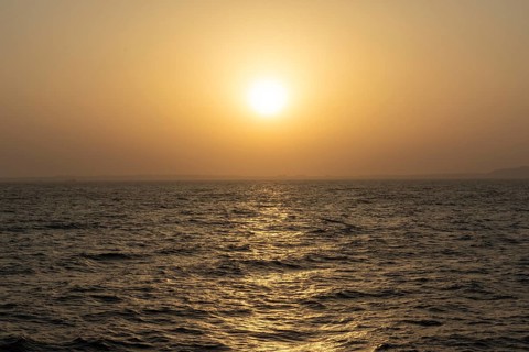 Background image, setting sun with silhouette of land, water surface in evening light, waves in the