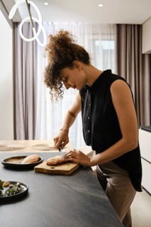 A woman is focused on cutting duck fat in a kitchen. Natural light fills the space, enhancing the