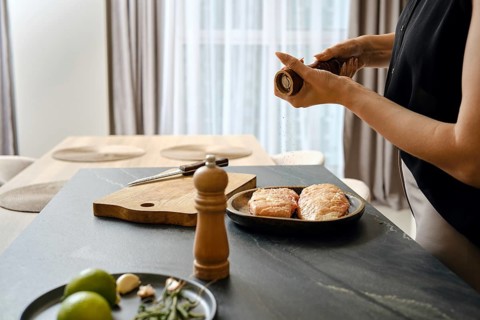 In a contemporary kitchen, a person is seasoning duck fillets with pepper while preparing dinner