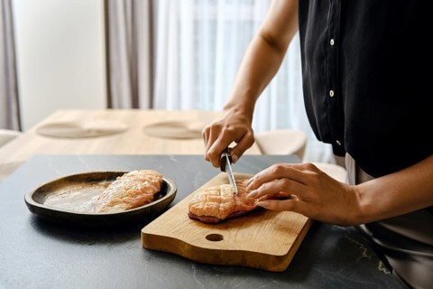 A person skillfully slices fresh duck fillets on a wooden cutting board in a modern kitchen