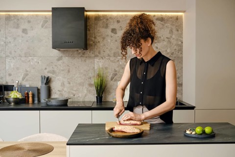 In a sleek, contemporary kitchen, a woman with curly hair skillfully chops ingredients on a wooden