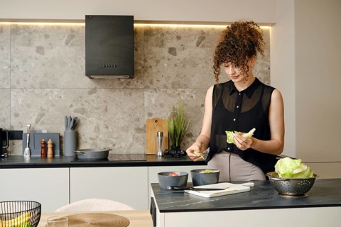 Woman with curly hair prepares a fresh salad in a contemporary kitchen. She is tearing lettuce with