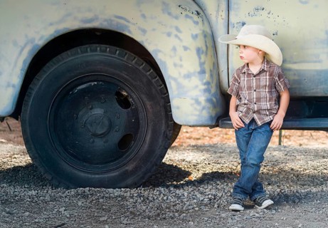 Young boy wearing cowboy hat relaxing leaning against antique truck