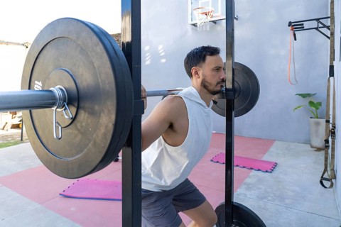 Focused male athlete lifting weights and performing squats in a home gym, showcasing strength and