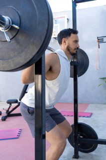 Focused male athlete is strengthening his legs by performing squats with a weighted barbell in a