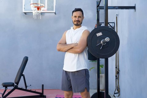 Sportsman with crossed arms is posing next to a weightlifting rack in a private outdoor gym,