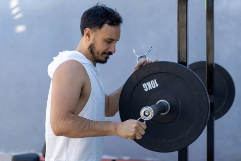 Focused male athlete meticulously secures weight plates onto a barbell, preparing for an intense