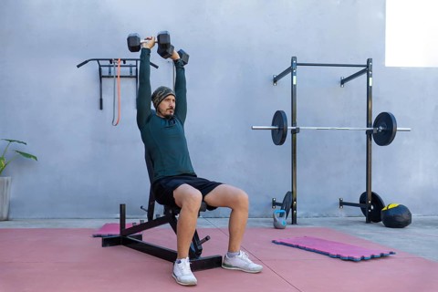 Focused athlete lifting dumbbells while seated on a bench in an outdoor gym, demonstrating strength