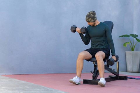 Focused athlete performs bicep curls with dumbbells, seated on a weight bench, showcasing
