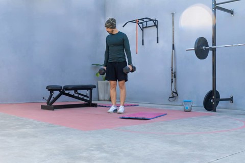 Young sportsman lifting two black dumbbells while engaging in a workout in a private outdoor gym,
