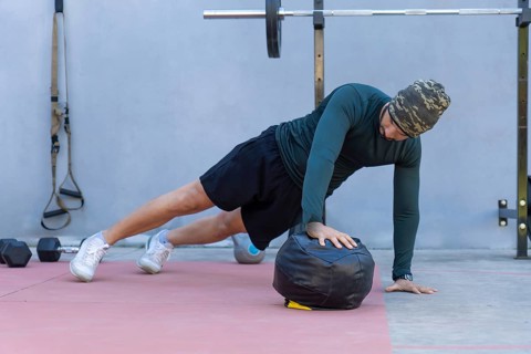 Focused male athlete wearing a beanie performing one-handed push-ups on a medicine ball in an